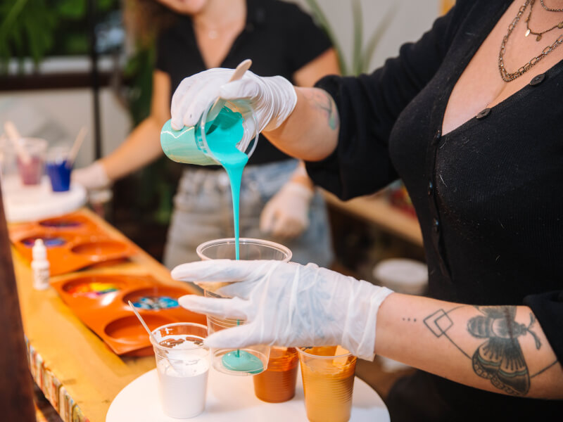 A woman is pouring colourful paint into a cup 